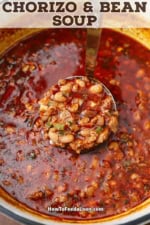 A person using a metal ladle to lift a serving of chorizo and bean soup from a pot of the simmering soup.
