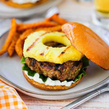 A curry turkey butter with grilled pineapple sitting a plate and is garnished with a dill yogurt sauce and green leaf lettuce.