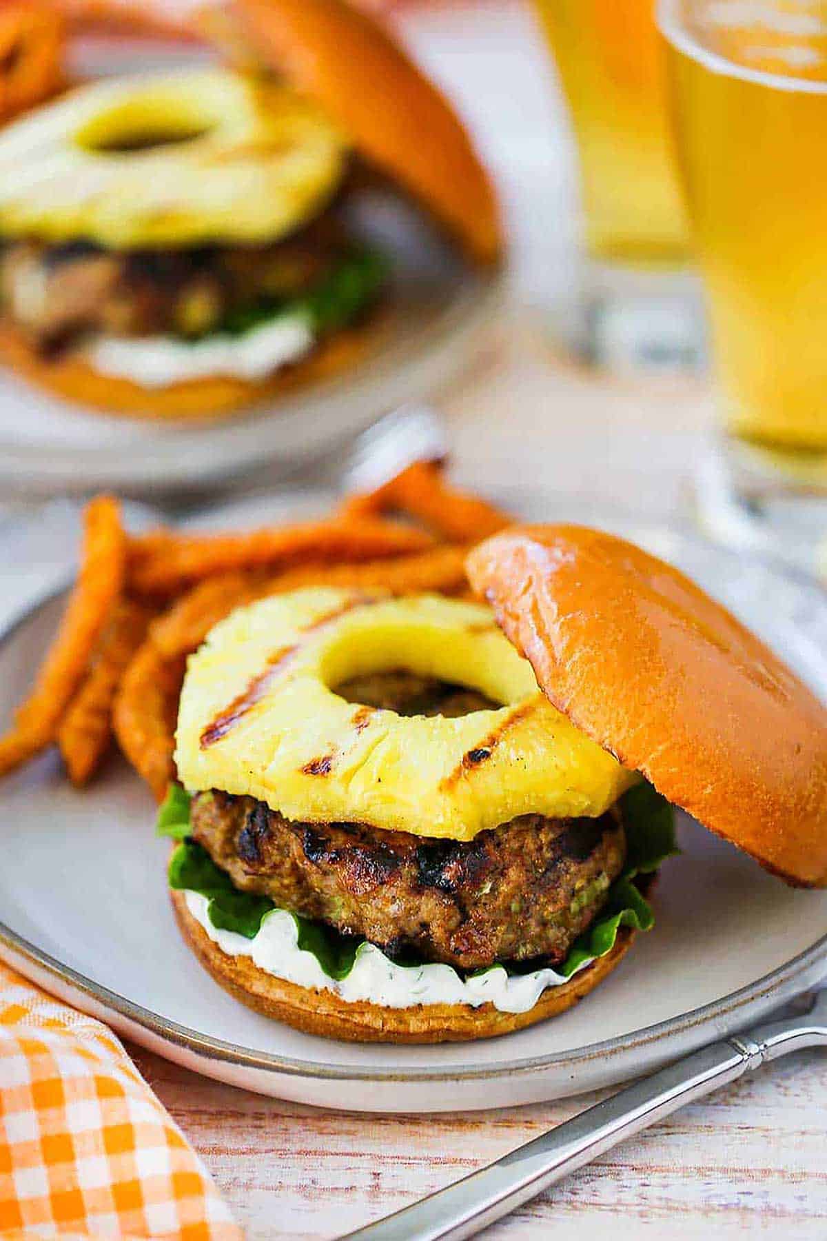 Two plates filled with curry turkey burgers with grilled pineapple sitting next to a pile of sweet potato French fries.