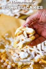 A person holding a portion of a homemade funnel cake in his hand over the rest of the funnel cakes below.