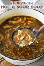 A person using a large wooden ladle to transfer homemade Chinese hot and sour soup from a large pot into a festive Asian soup bowl.
