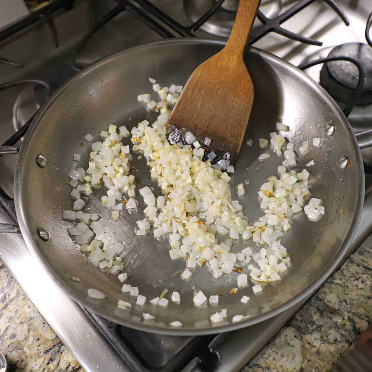 A large silver skillet filled with chopped onions that are being sautéed on a gas stove.