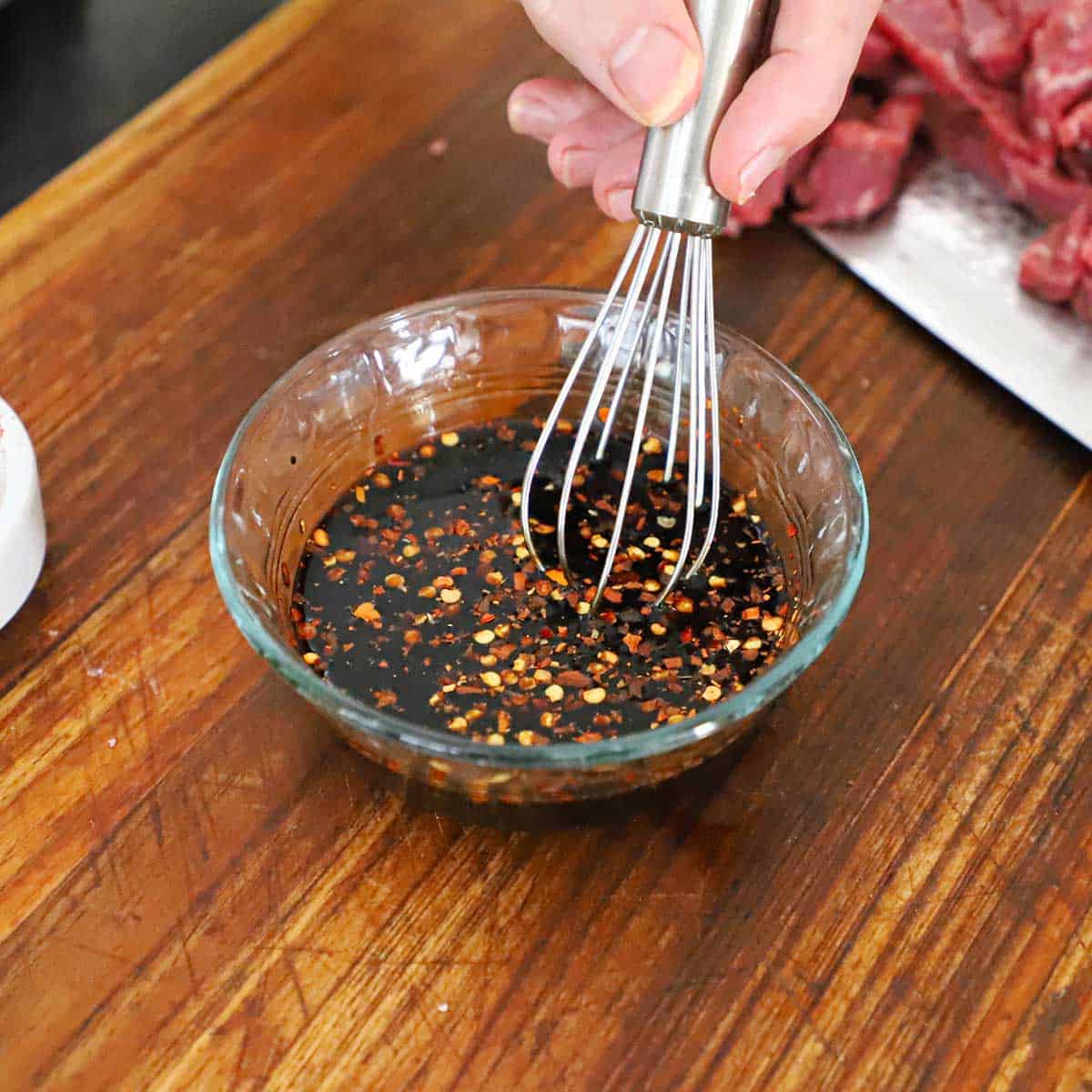 A person using a small whisk to combine a sauce for crispy chili beef.