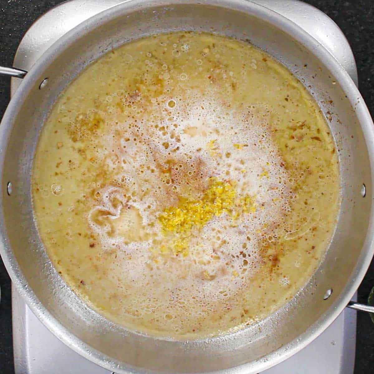 A large stainless steel skillet filled with simmering butter, white wine, and garlic.