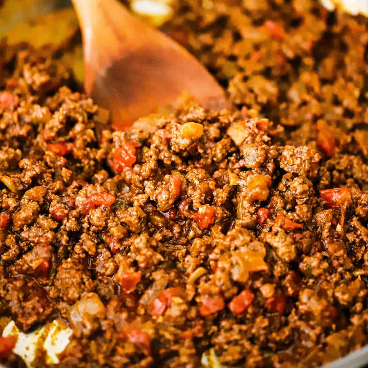 A close-up view of Tex-Mex taco meat being stirred in a skillet with a large wooden spoon.