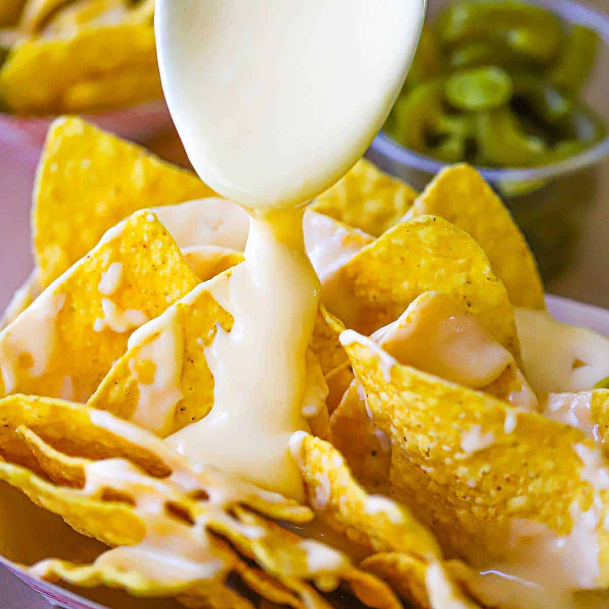 A spoon being used to drizzle easy homemade nacho sauce over a basket-full of corn tortilla chips.