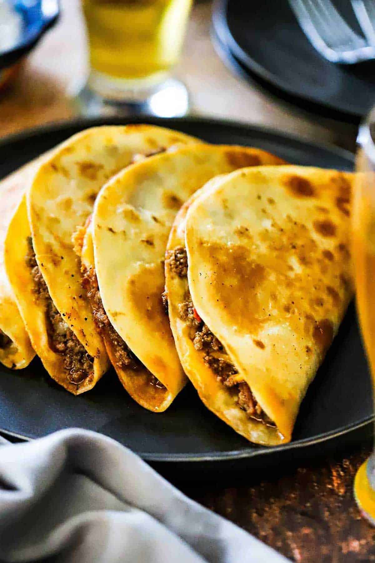 A black dinner plate filled with one taco quesadilla stacked one after another.