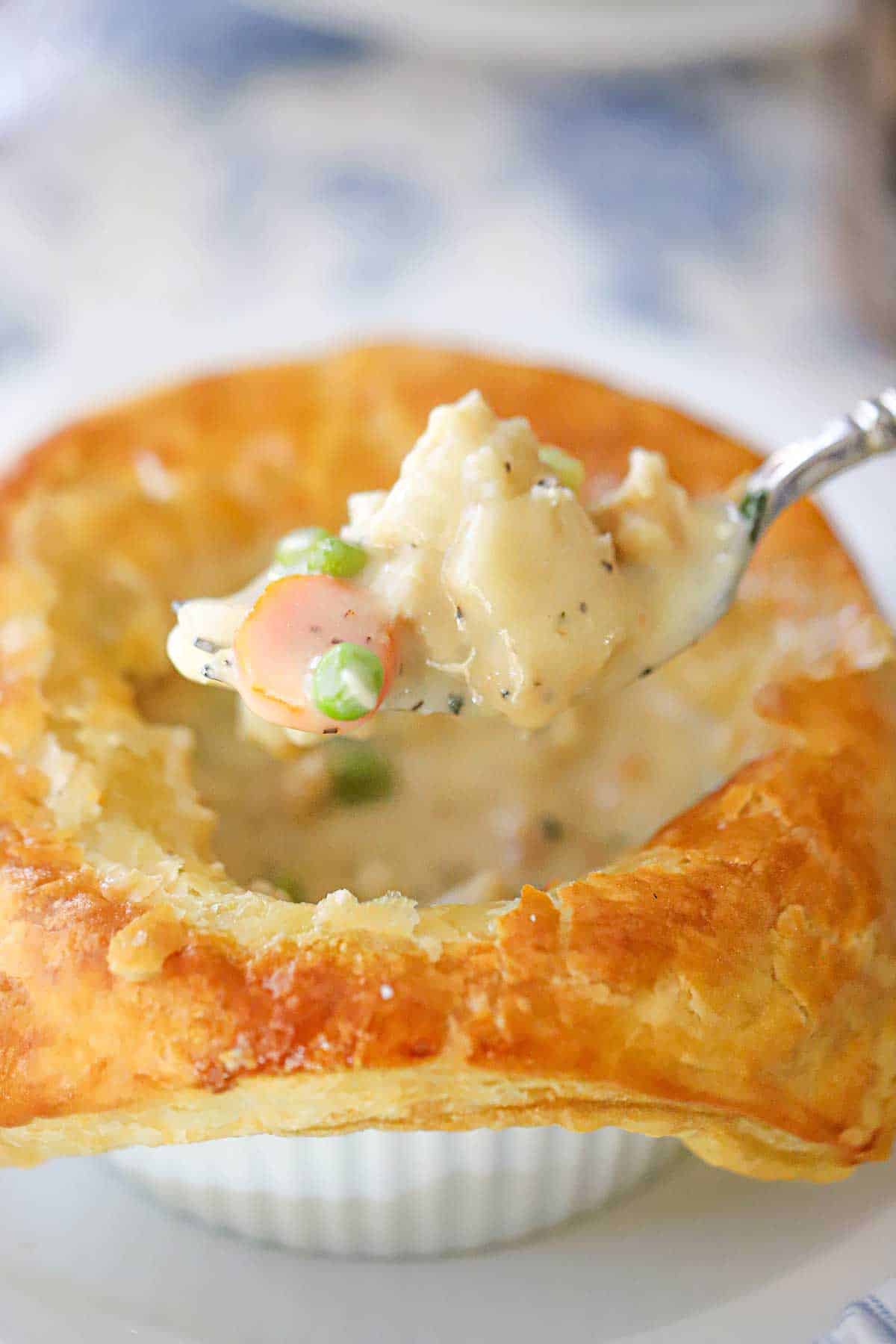A person using a fork to raise the filling from the inside of an opened up leftover turkey pot pie with buttery puff pastry.