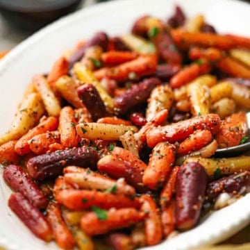 A close-up view of an oval white platter filled with roasted baby carrots with herb vinaigrette and topped with chopped Italian parsley.