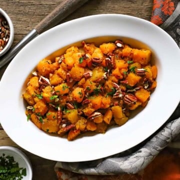 An overhead view of a white oval serving dish filled with Maple-Glazed Butternut Squash with Pancetta and Herbs.