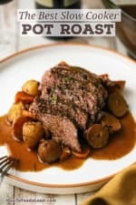 A white dinner plate filled with a serving of the best slow cooker pot roast with vegetables and brown gravy.