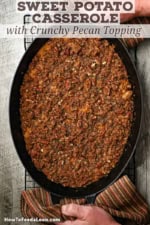 An overhead view of an freshly baked sweet potato casserole with crunchy pecan topping being place on a baking rack by a person using autumnal cloth linens to grip the handles.