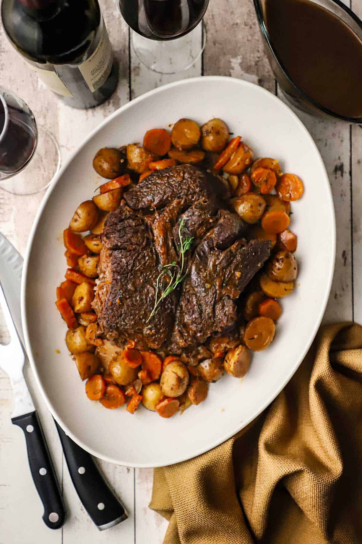 An overhead view of the best slow cooker pot roast on a platter surrounded by slow cooked potatoes and carrots.