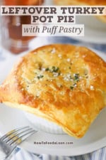 A leftover turkey pot pie with puff pastry resting untouched on a white dinner plate.