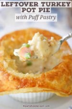 A person using a fork to raise the filling from the inside of an opened up leftover turkey pot pie with buttery puff pastry.