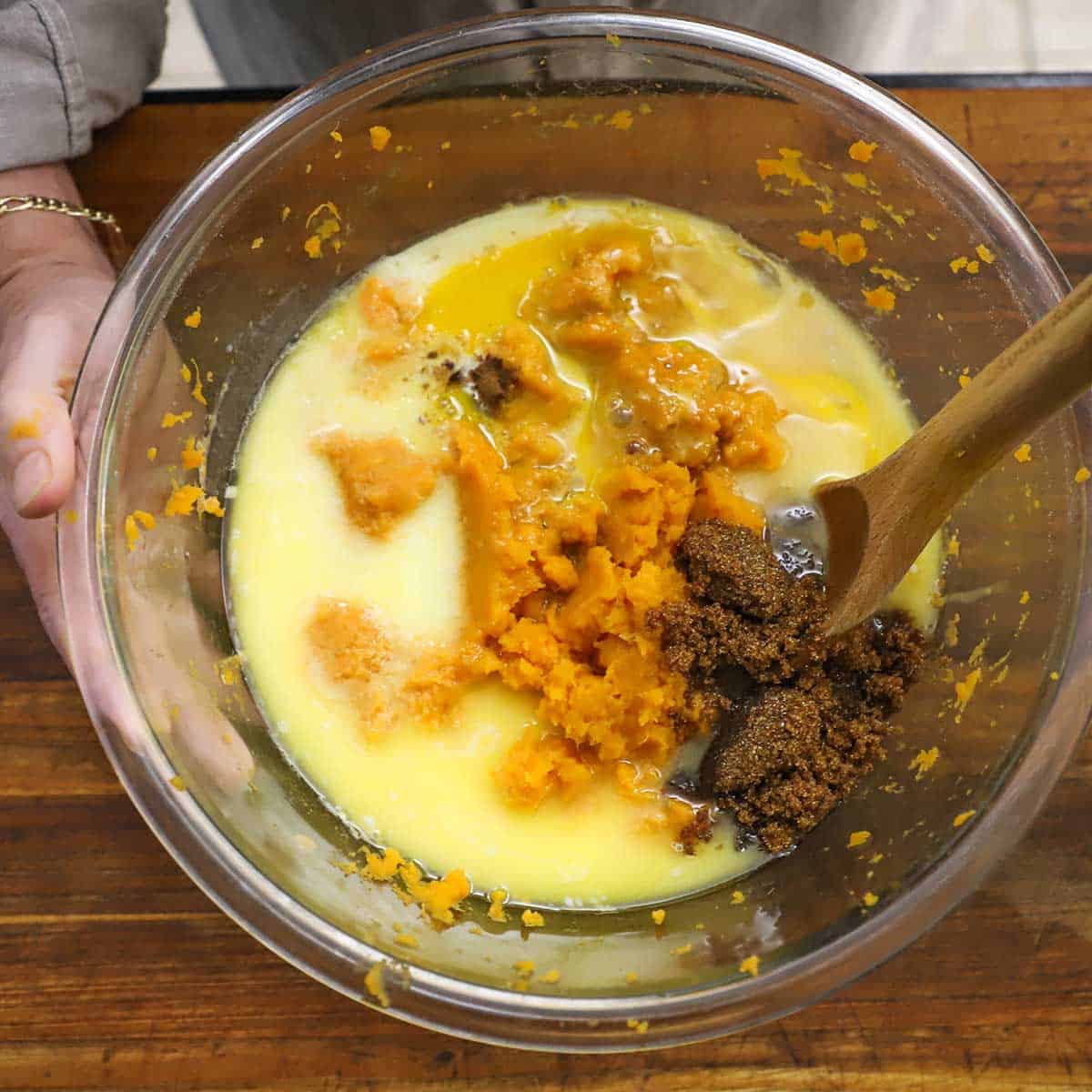 A person stirring mashed sweet potatoes with melted butter, brown sugar, granulated sugar, milk, and eggs.