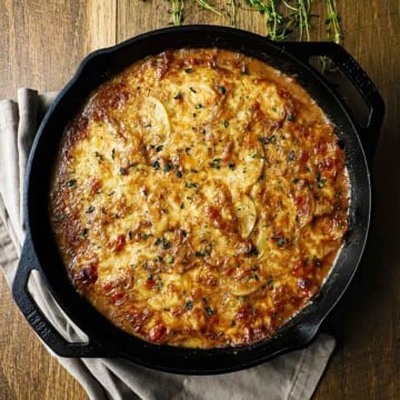 An overhead view of a large cast-iron skillet filled with French onion au gratin potatoes.