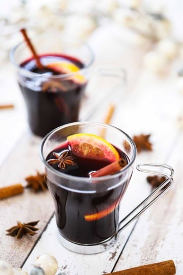 Two glass mugs filled with mulled wine (gluewein) garnished with an orange wedge, star anise, and a cinnamon stick.