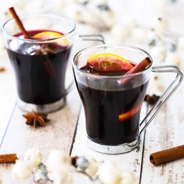 Two glass mugs filled with mulled wine (gluewein) garnished with an orange wedge, star anise, and a cinnamon stick.