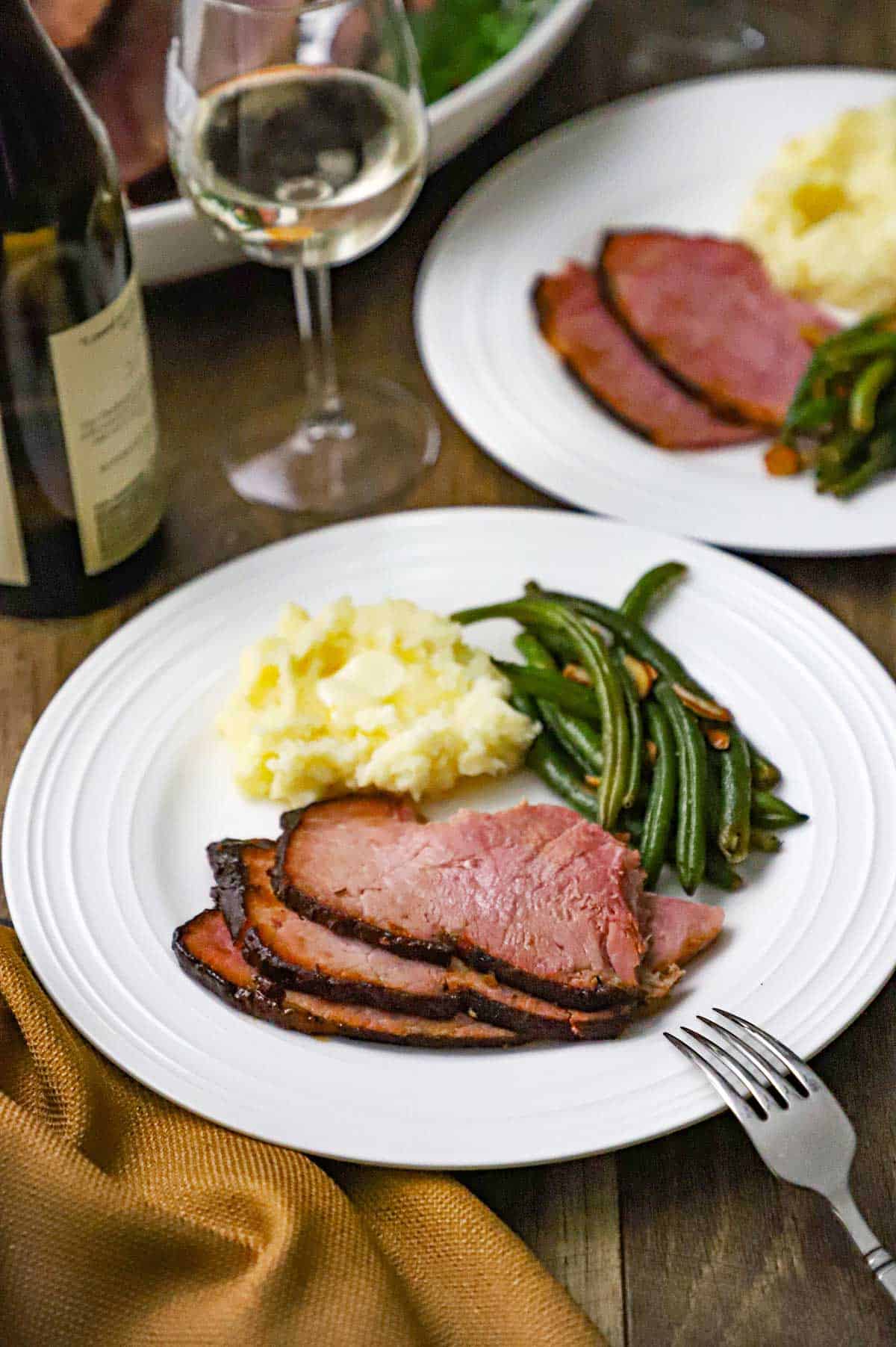 A white dinner plated filled with three slices of honey mustard glazed smoked turkey, mashed potatoes, and green beans almondine.