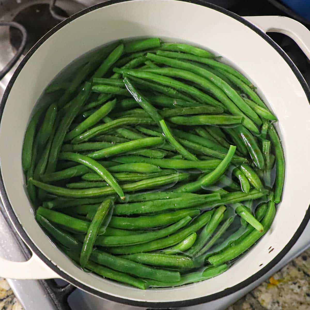 A large white pot filled with fresh green beans simmering in water on a gas stove.