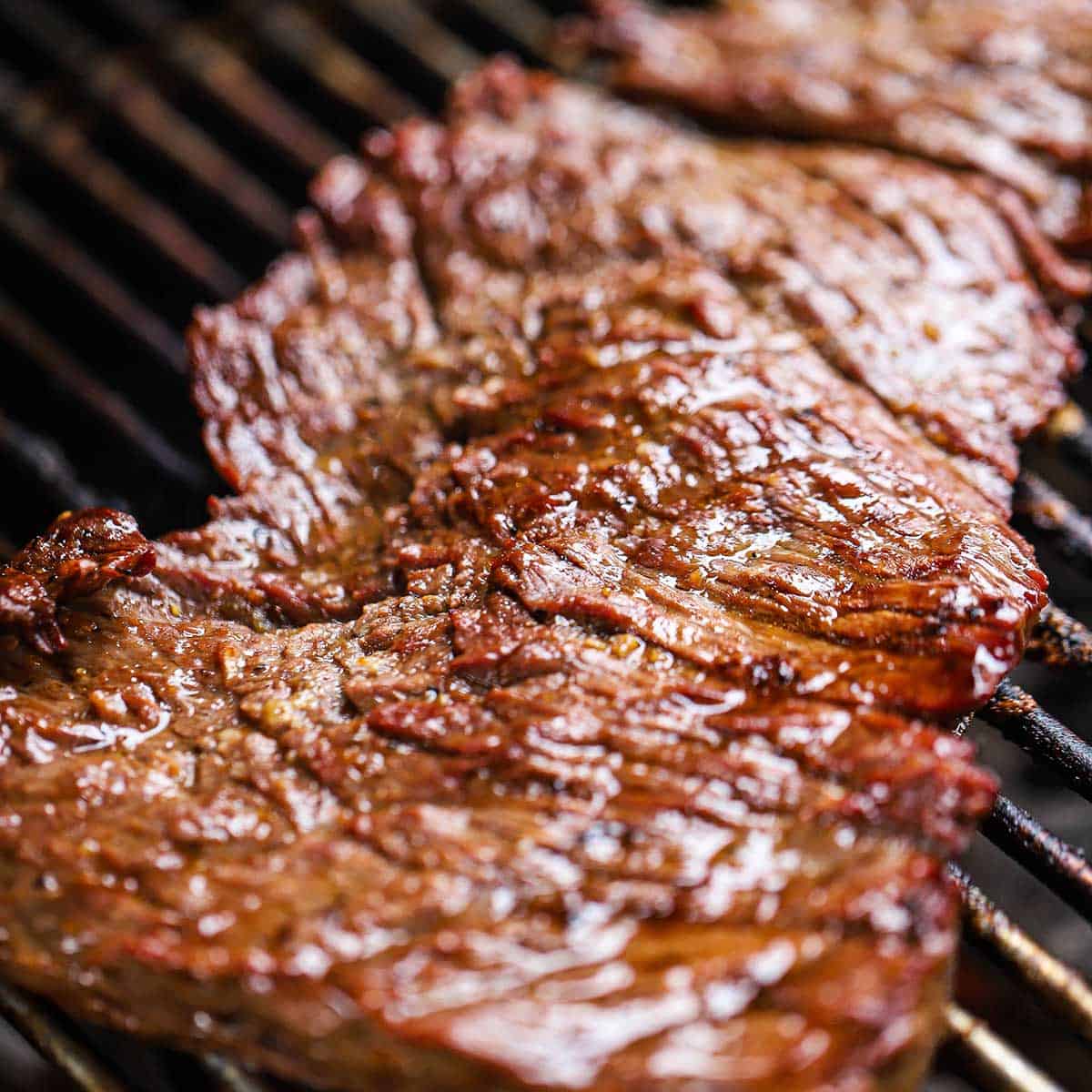 A close-up view of marinated skirt steak being grilled on a gas grill.
