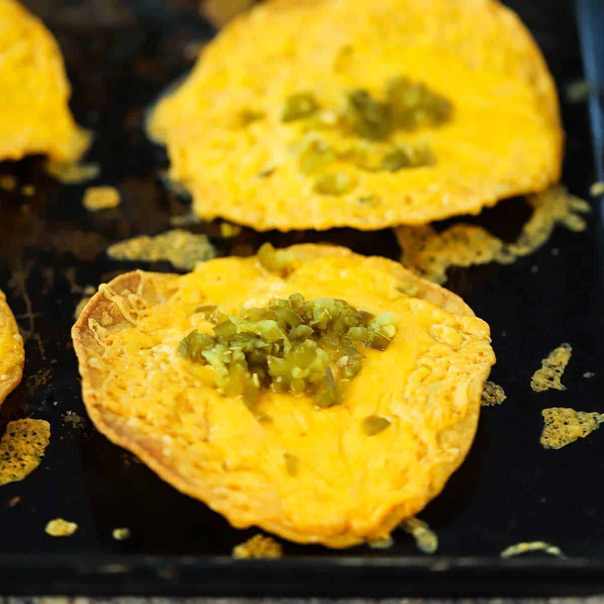 A close-up view of two classic nachos topped with chopped jalapeños that have just come out of the oven.